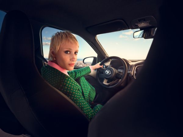 Interior image from rear of Chili Red Aygo X with driver looking back over her shoulder